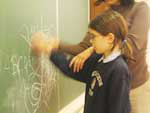 betitelt „schreiben“ zeigt ein Mädchen im Volksschulalter, das Kreise auf eine Tafel malt, mit einer AT Lehrerin, die ihren Arm führt.