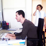Betitelt „vorher“ zeigt einen Mann am Computer-Arbeitsplatz mit stark nach vorne gekrümmter Wirbelsäule, die Tastatur liegt sehr weit weg von ihm, die Unterarme sind am Tisch aufgestützt, der Hals nach vorne gestreckt.