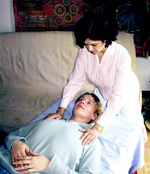 betitelt „Alexander-Technik Unterricht im Liegen“, zeigt A.M. mit den Händen auf den Schultern einer am Rücken liegenden Frau.